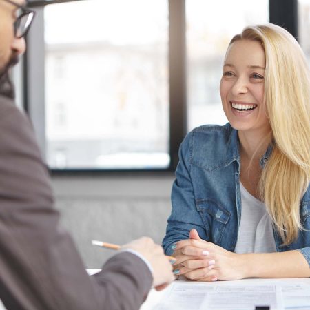 Happy blonde female manager in fashionable clothes has pleasant conversation with male colleague, discuss successful strategy for startup, chaeck list of affairs, consult new project together