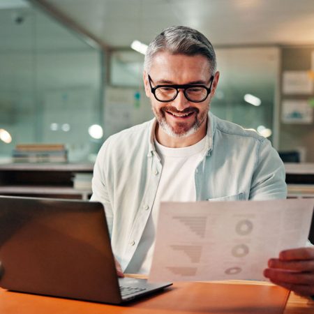 Smile, laptop and documents with business man in office for budget research, planning and graph. Profit chart, account review and paperwork with person in agency for finance, balance and growth.