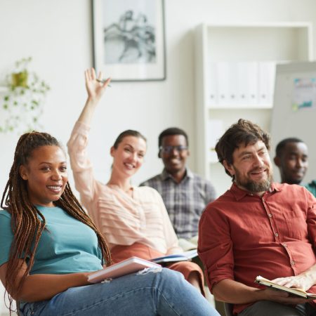 Multi-ethnic group of people raising hands while answering questions during training seminar or business conference in office, copy space